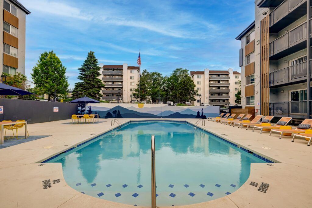 Apartment pool with lounge chairs, mural backdrop, and building in the background.