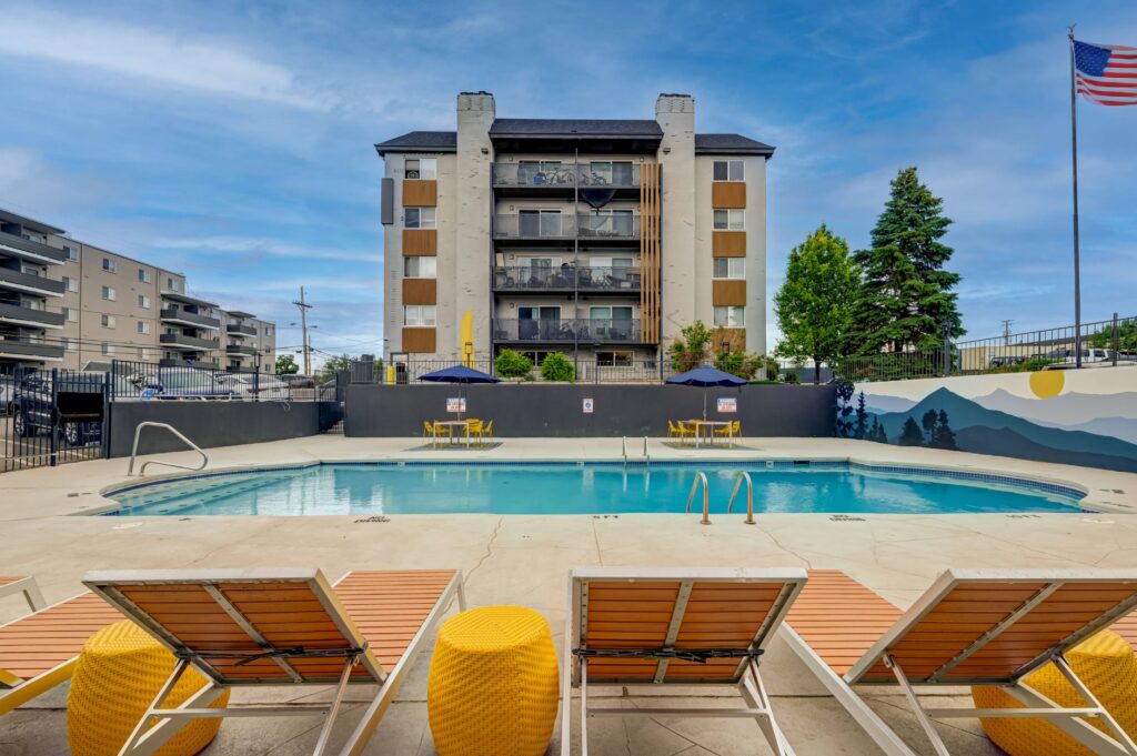 Apartment pool with lounge chairs, mural backdrop, and building in the background.